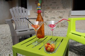 Two martini glasses on a green table, a bottle of brown liquid, and a bowl of fruit. - La Chèvrerie - MARCAY - Gîte (MARCAY)