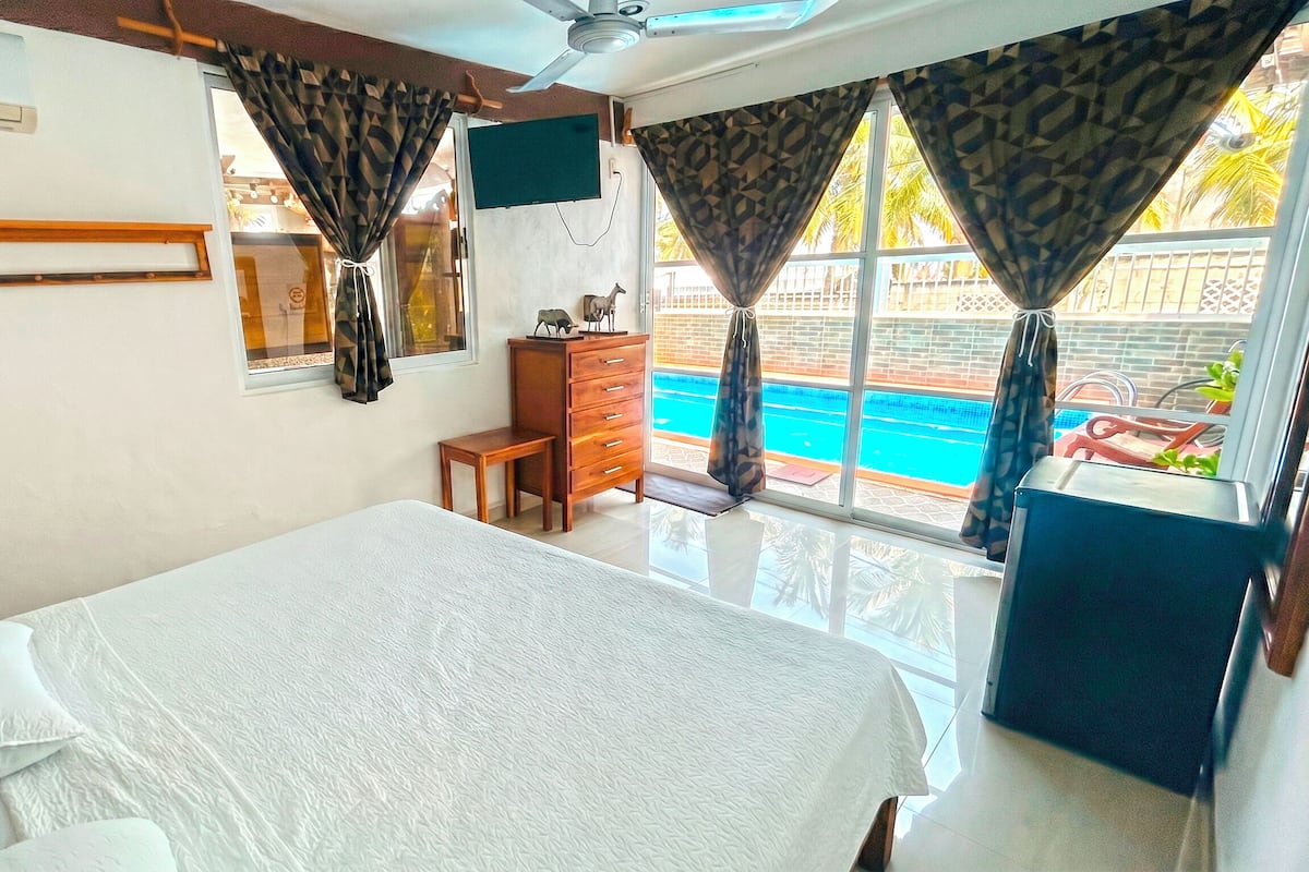 Ein Hotelzimmer mit Bett, Kommode, Fernseher und Blick auf einen Swimmingpool.