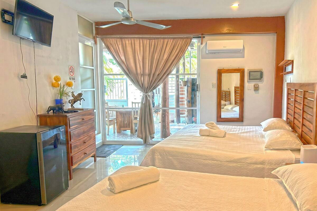 Ein Hotelzimmer mit zwei Betten, einem Fernseher, einem Schreibtisch und einem Fenster mit Vorhängen.