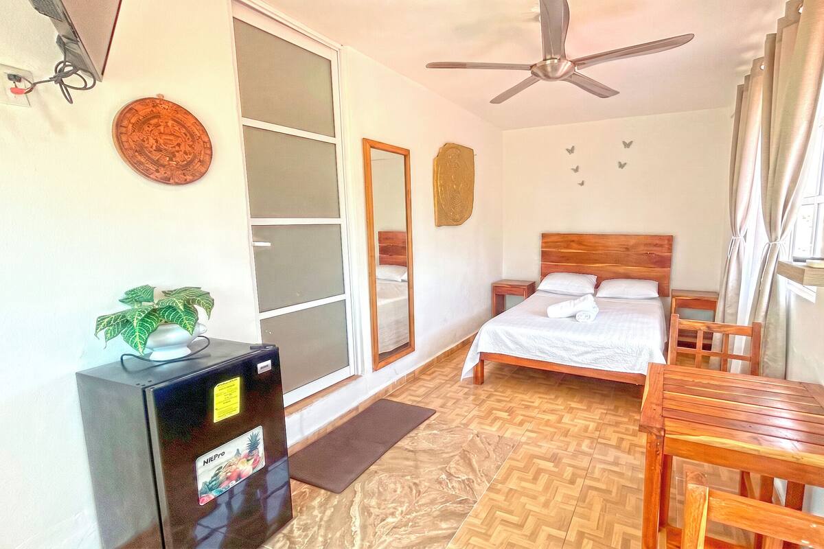 Ein Schlafzimmer mit einem Bett, einem Schreibtisch, einem Deckenventilator, einem Spiegel und einer Glastür.