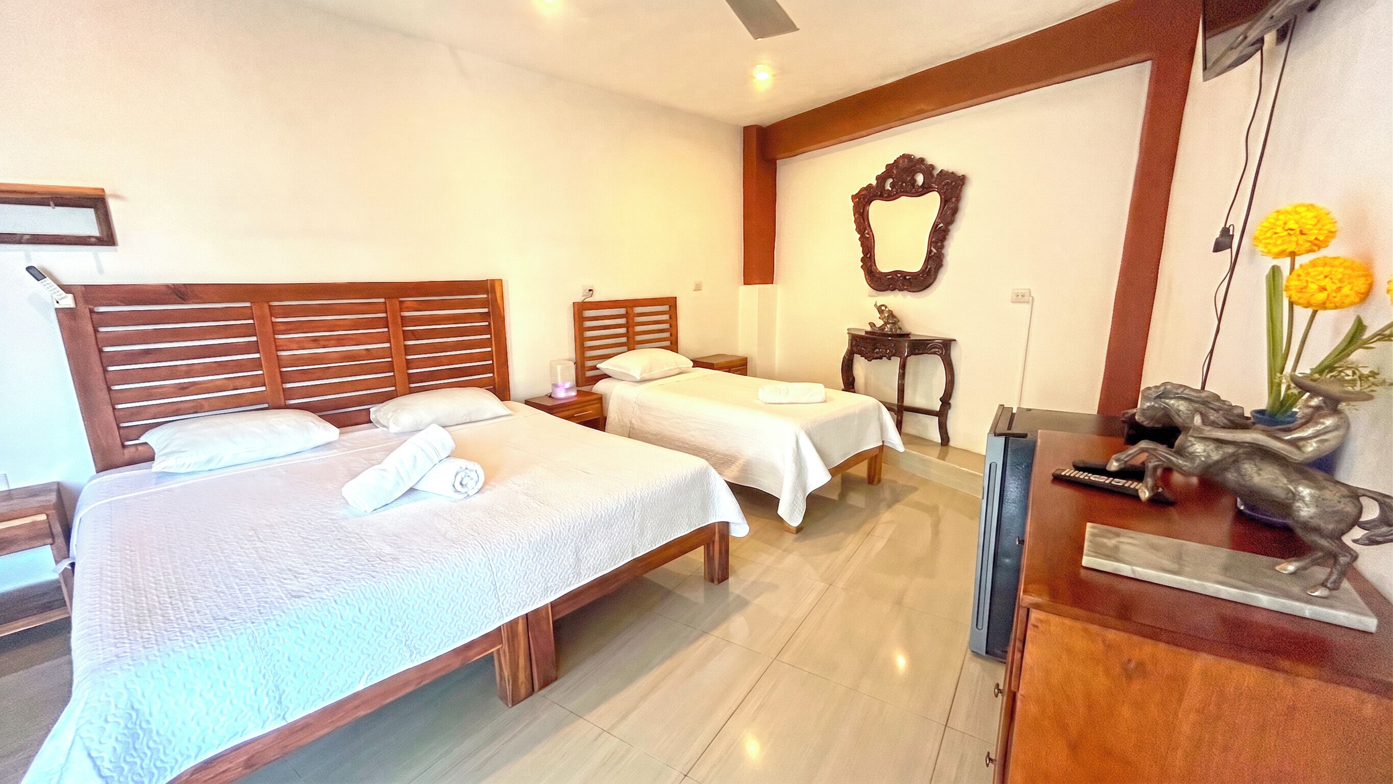 Habitación de hotel con dos camas, cabecero de madera, una mesita, un espejo y una estatua.