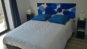 Un dormitorio con una cama, dos mesitas de noche y un ventanal con cortinas.