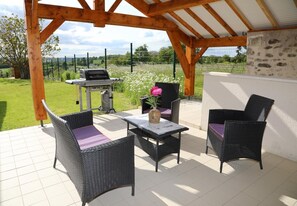 An outdoor patio with wicker furniture, a grill, and a view of the countryside. - Gîte Montgolfière - CHATELLERAULT (CHATELLERAULT)