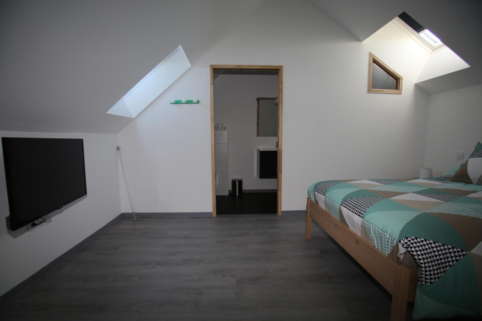A bedroom with a sloped ceiling, a bed with patterned bedding, a TV mounted on the wall, and a skylight.