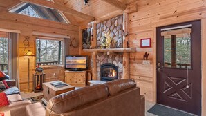 A log cabin interior with a stone fireplace, a television, a leather sofa, and a wooden door. - Rustic Ridge Cabin 104 - Private Woodland Retreat near Devil's Lake State Park (Merrimac)