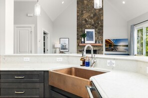 A modern kitchen with a copper sink, dark cabinetry, a stone accent wall, and a large window with a view. - New!!  Lakefront, Dock, Kayaks, Firepit & Game Room (Macon)