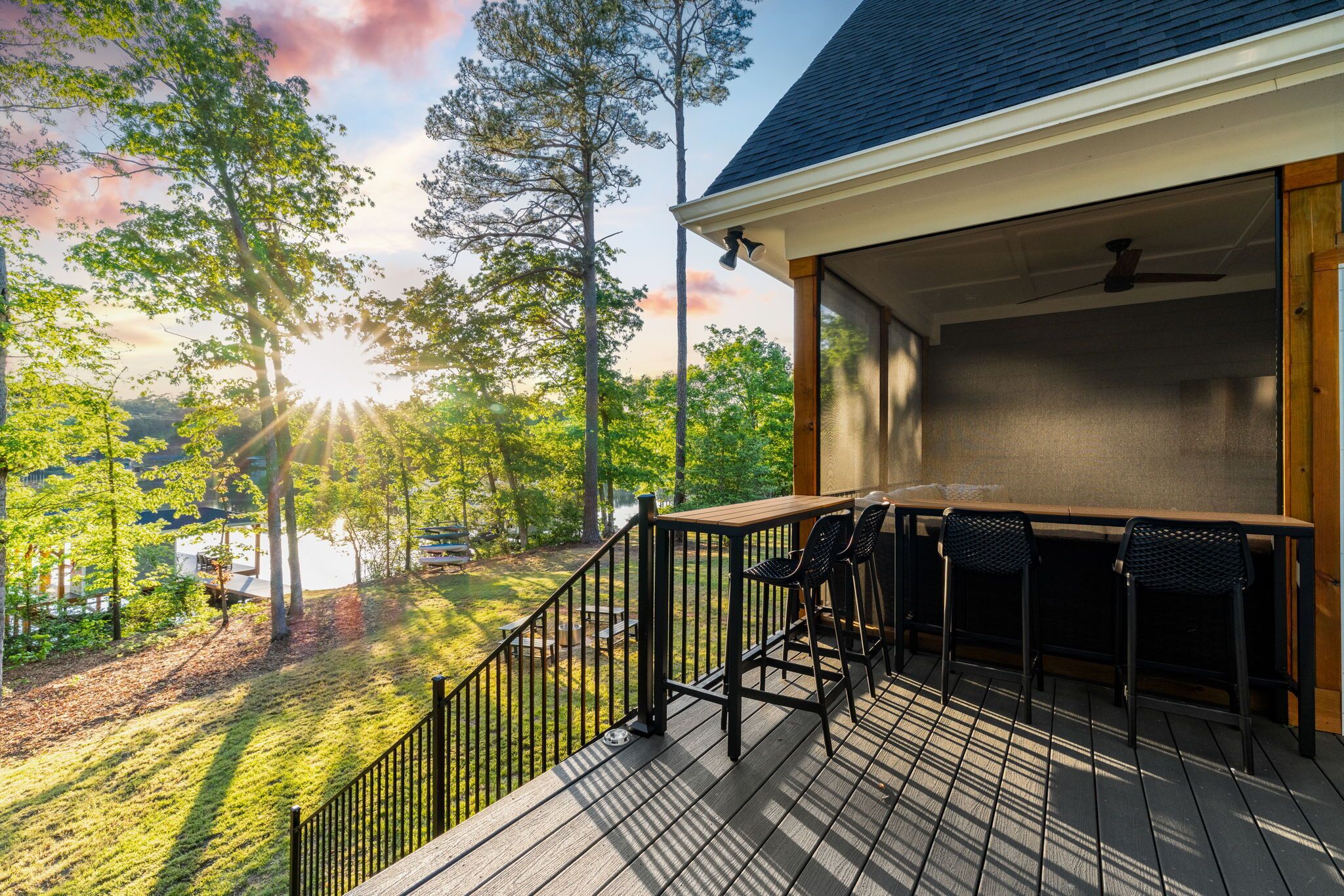A covered outdoor deck with a table and chairs, surrounded by trees and a view of a lake.