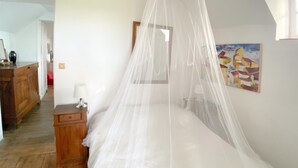 Quarto com cama de dossel, penteadeira de madeira, luminária de cabeceira e um quadro na parede.