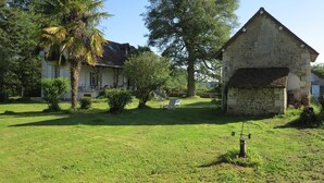 Um edifício de pedra com telhado inclinado, rodeado por um gramado bem cuidado e árvores.