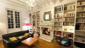 Uma sala de estar com lareira, estantes, um sofá e um candelabro.