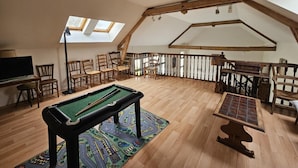 Een loft-stijl kamer met een pooltafel, houten stoelen, een biljartrek en een biljartkeu-rek.