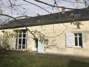 A stone building with a sloped roof, white shutters, and a small garden area with potted plants. - Le Pin de la Tour - SOSSAIS (SOSSAIS)