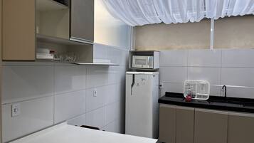 A kitchen with white cabinets, a microwave, a refrigerator, and a sink.