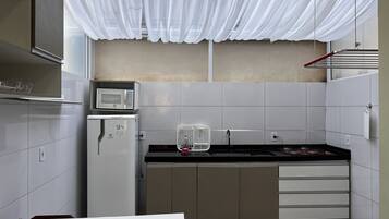 Una cocina compacta con gabinetes blancos, microondas, refrigerador, estufa a gas y un lavamanos.