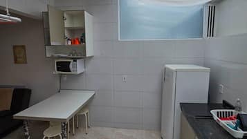 Een kleine keuken met een eettafel, een magnetron, een koelkast en een raam met uitzicht.