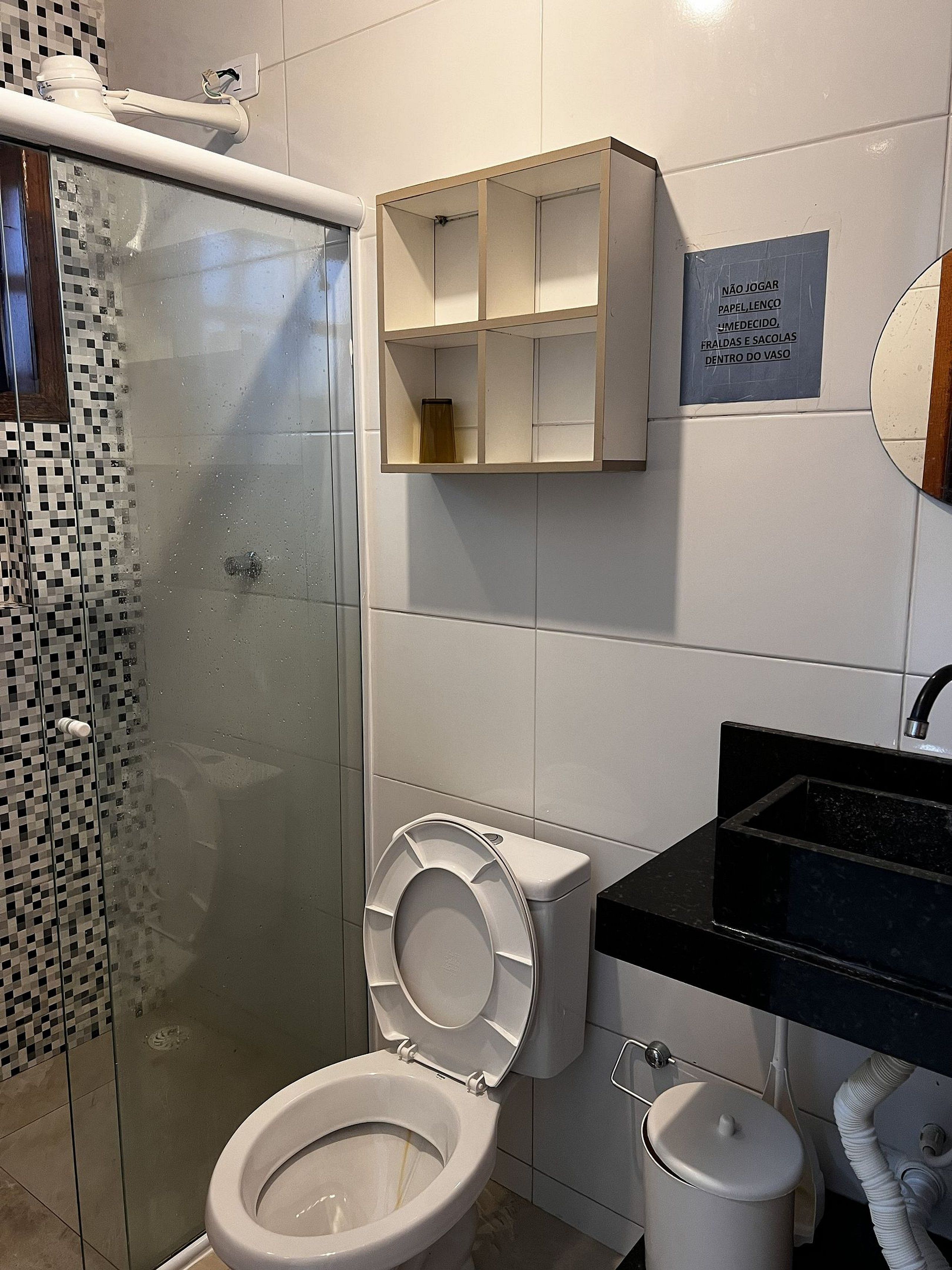 Un baño con inodoro, ducha, lavamanos y un mueble con un cartel.