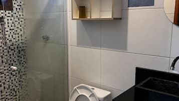 Un baño con inodoro, ducha, lavamanos y un mueble con un cartel.