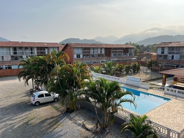 A hotel with a swimming pool, palm trees, and a view of mountains. - Reserve MV2 (Ubatuba)