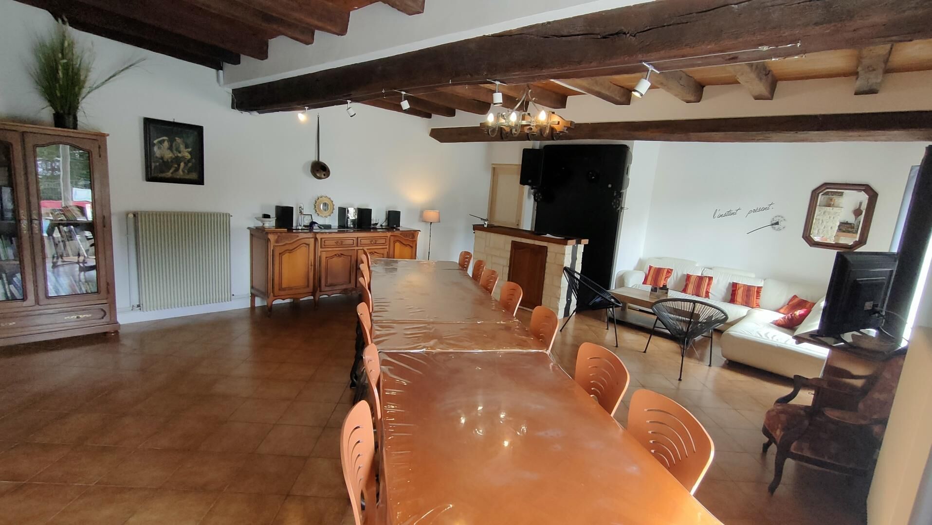 A dining area with a long wooden table and chairs, a radiator, a cabinet with speakers, and a sofa with cushions.