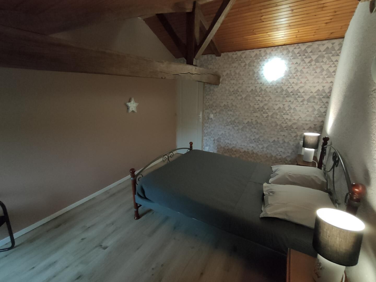 A bedroom with a bed, wooden beams, a star decoration, patterned wallpaper, and bedside lamps.