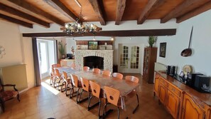 A spacious dining area with a large wooden table and orange chairs, a fireplace, and a kitchen area with wooden cabinets and a radiator. - Gîte Victor - SAINT-MARTIN-LA-PALLU (SAINT-MARTIN-LA-PALLU)
