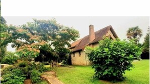 Ein kleines Steinhaus mit geneigtem Dach, umgeben von üppiger Vegetation und Bäumen.