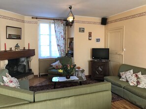 A living room with a fireplace, sofa, television, and a window with curtains. - La Forge de Louis - SAINT-MACOUX VAL DE COMPORTE (SAINT-MACOUX VAL DE COMPORTE)
