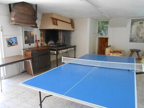 A ping pong table in a room with a tiled floor, a wooden table, and a poster on the wall. - La Forge de Louis - SAINT-MACOUX VAL DE COMPORTE (SAINT-MACOUX VAL DE COMPORTE)