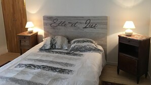 Ett sovrum med en säng, två sängbord med lampor, en garderob i trä och en sänggavel med en namnskylt.