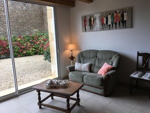 A living room with a sofa, a coffee table, a painting, and a view through a glass door. - L'Ammonite - CHAUNAY (CHAUNAY)