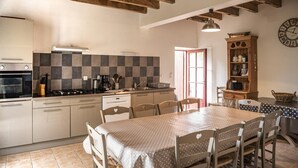 A kitchen with a stove, oven, and checkered backsplash. There is a dining table with chairs and a clock on the wall. - La Maison d'Irène - ANCHE (ANCHE)