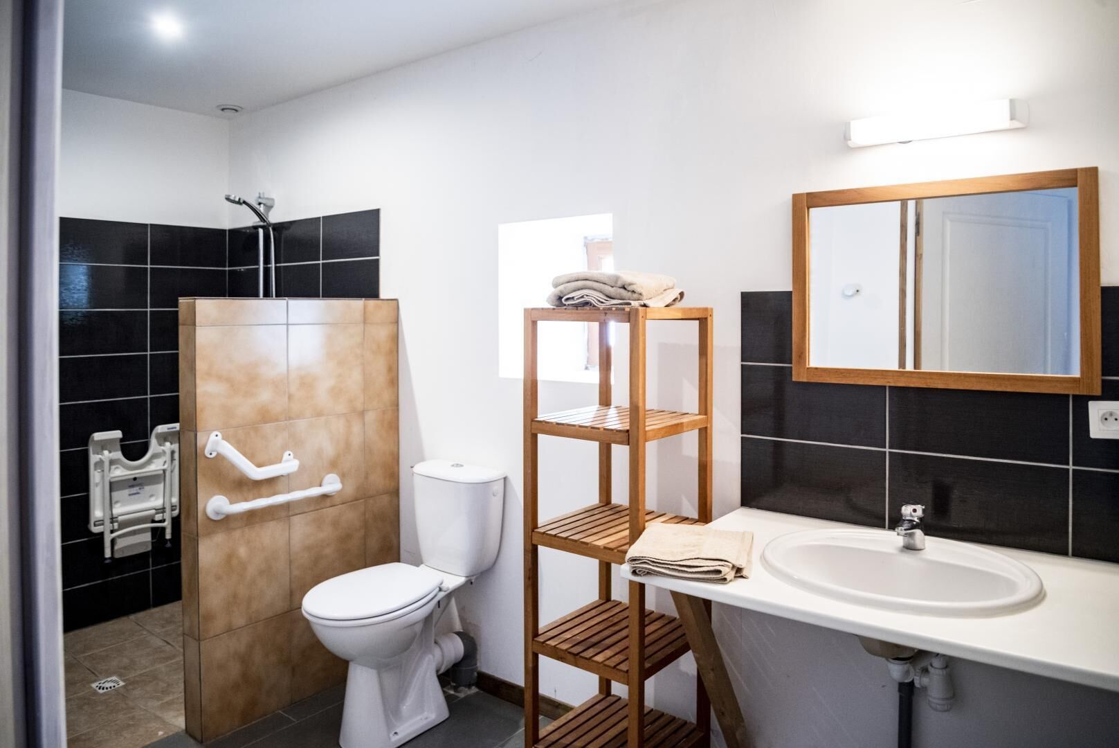 Et badeværelse med toilet, brusebad, håndvask og en træhylde.
