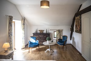 Une pièce avec deux fauteuils bleus, une table ronde ornée d’un pot de fleurs, une commode en bois foncé et une porte blanche.