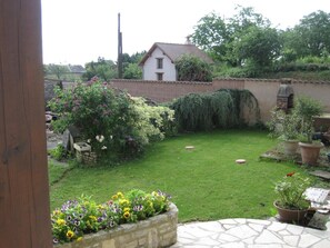 Un jardín trasero con césped, un muro de ladrillo, una valla de madera y una casa al fondo.