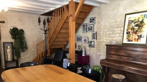 Een eetruimte met een houten tafel, een trap, een piano en ingelijste foto's aan de muur.