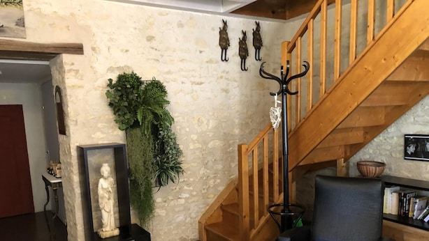 Een kamer met een stenen muur, een houten trap, een zwarte lederen fauteuil, een beeld en een plant.