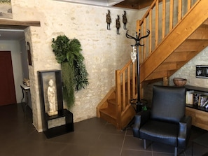 A room with a stone wall, a wooden staircase, a black leather chair, a statue, and a plant. - Le Clos Constance - SAINT-MARTIN-LA-PALLU (ETABLES) (SAINT-MARTIN-LA-PALLU (ETABLES))