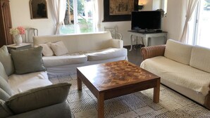 Een woonkamer met een bank, een salontafel, een televisie en een groot raam met gordijnen.