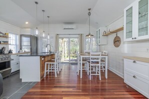 A modern kitchen with white cabinetry, a central island, pendant lighting, and a dining area with white chairs. - Downtown Cottage Retreat, Steps to Beach, Dining & Shops. Sleeps 4! (Ogunquit)