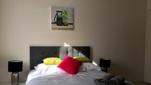 Een opgemaakt bed met witte lakens, een rood kussen en twee lampen aan weerszijden.