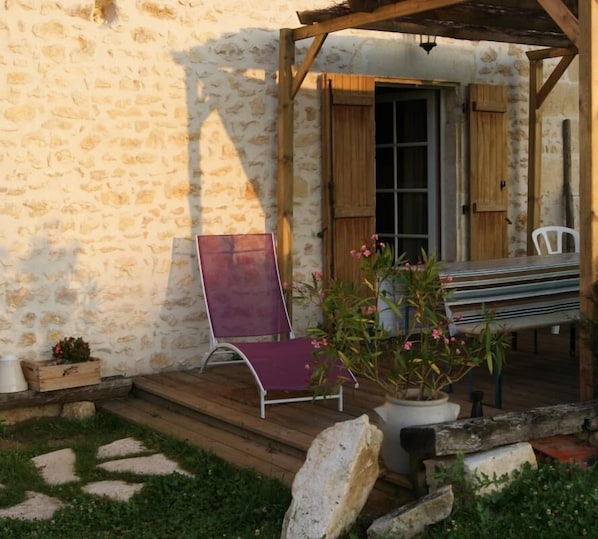 A stone building with a wooden porch, a purple chair, a bench, and potted plants. - Le Gîte de la Roche - ANTIGNY (ANTIGNY)