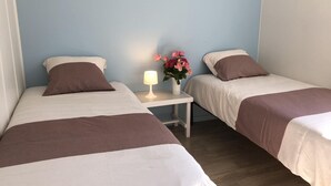 Una habitación con dos camas, una mesita de noche con lámpara y un jarrón con flores.
