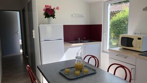 Cocina compacta con refrigerador, microondas y lavabo. Hay una mesa con jugo de naranja y un florero con flores en la pared.