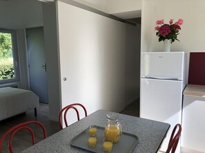 Eine moderne Küche mit einem Kühlschrank, einem Esstisch mit Stühlen und einem Fenster mit Blick auf Grünflächen.