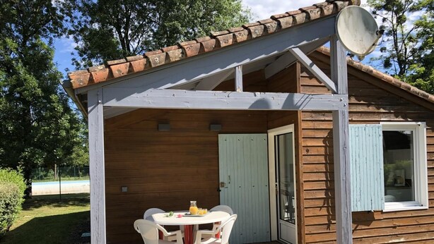 Una cabaña de madera con un porche cubierto, una mesa con sillas y una antena parabólica.