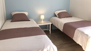 Una habitación con dos camas individuales, una mesita de noche con lámpara y suelo de madera.