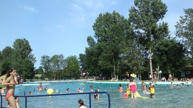 Piscina pública con varias pistas de natación, rodeada de árboles y un cielo despejado.