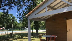 Un espacio de estar al aire libre techado con mesa y sillas, una terraza de madera y vistas a una piscina y árboles.