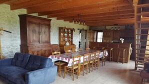 Una zona de menjador amb taula i cadires de fusta, un sofà i una cuina al fons.