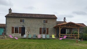 Una casa de pedra amb teulada de teules, un porxo de fusta i un jardí en verd.